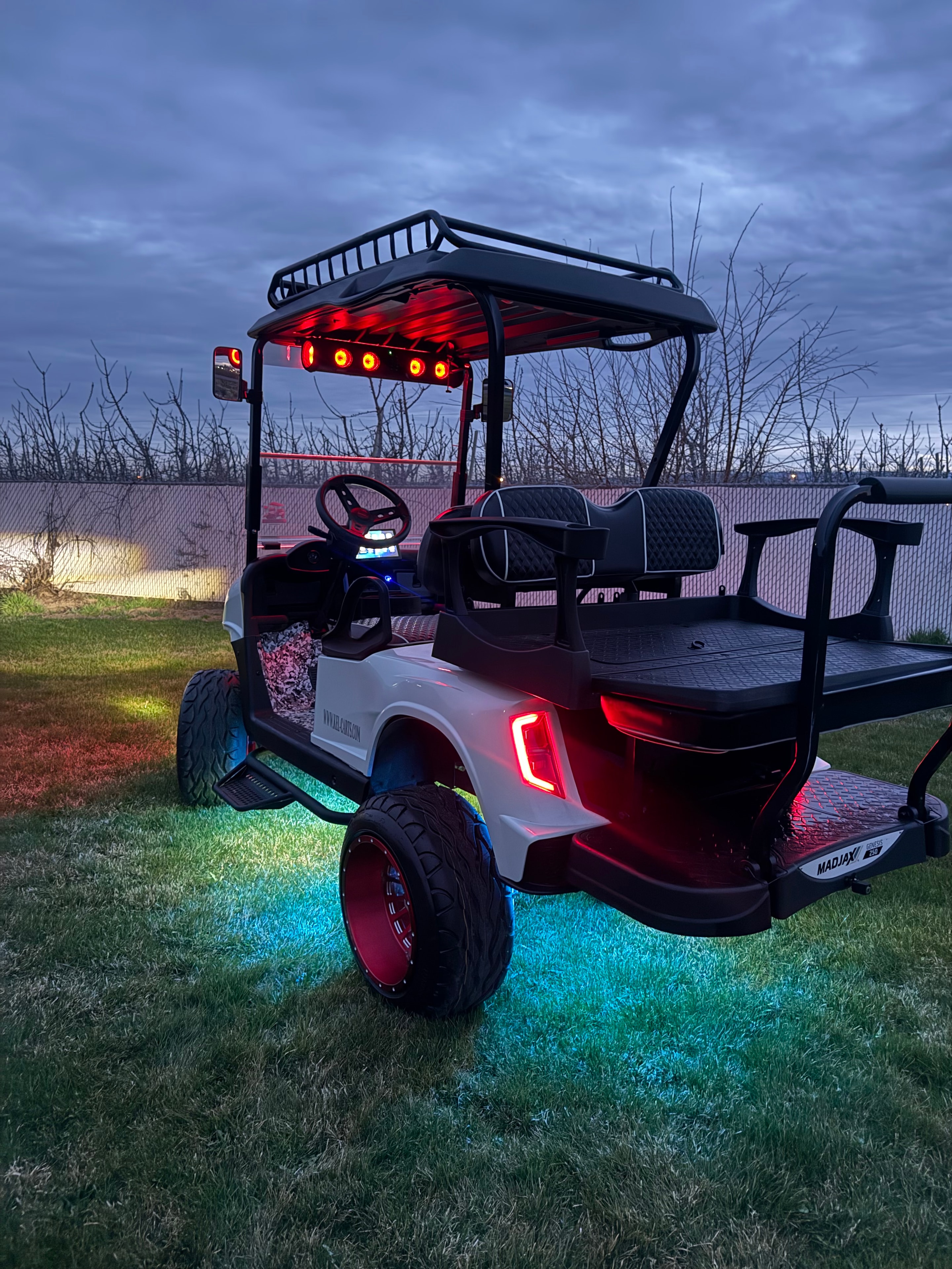 Cream custom golf cart with red wheels and illuminated underglow at dusk