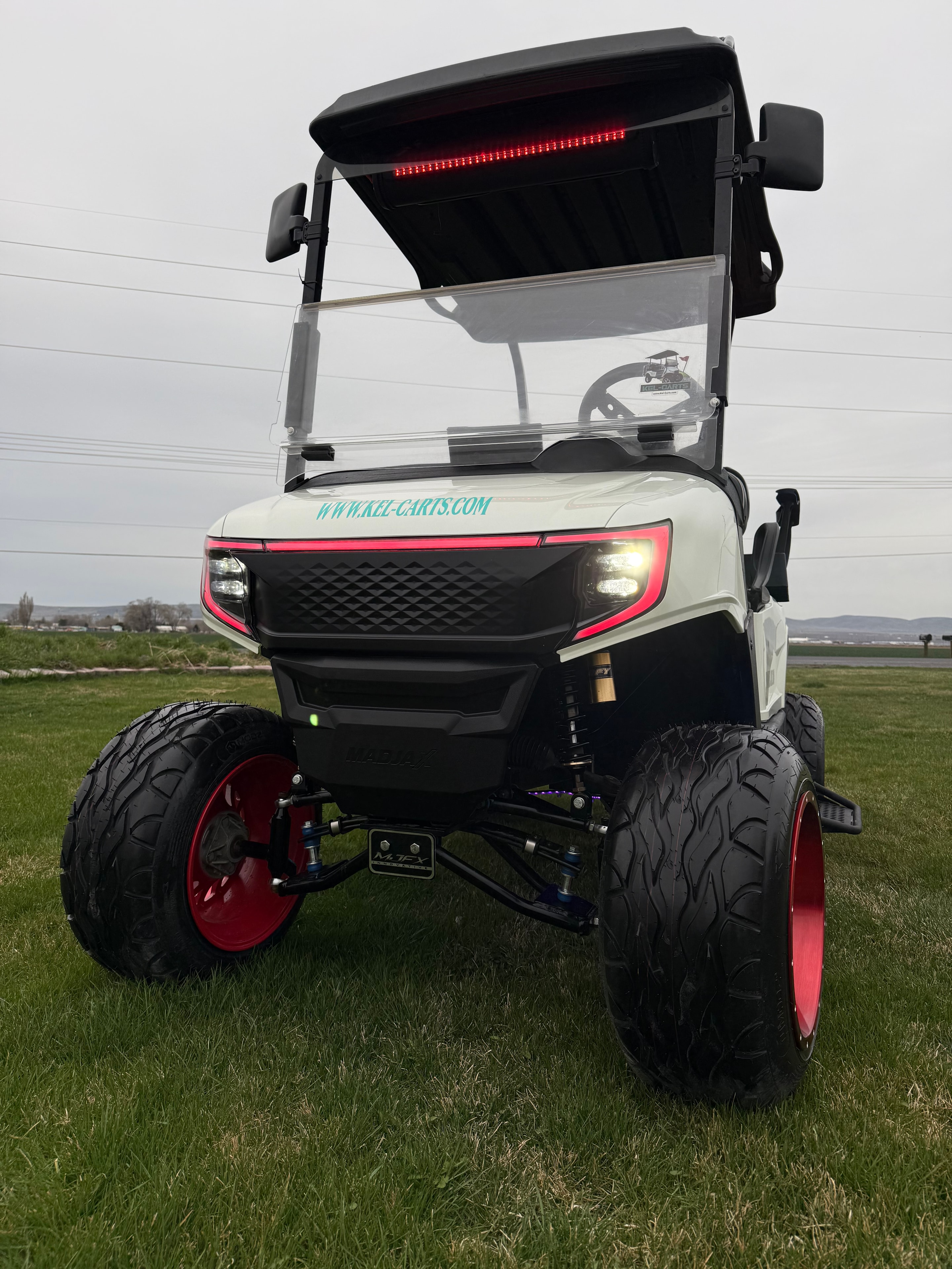 Cream off-road golf cart with red wheels and illuminated headlights