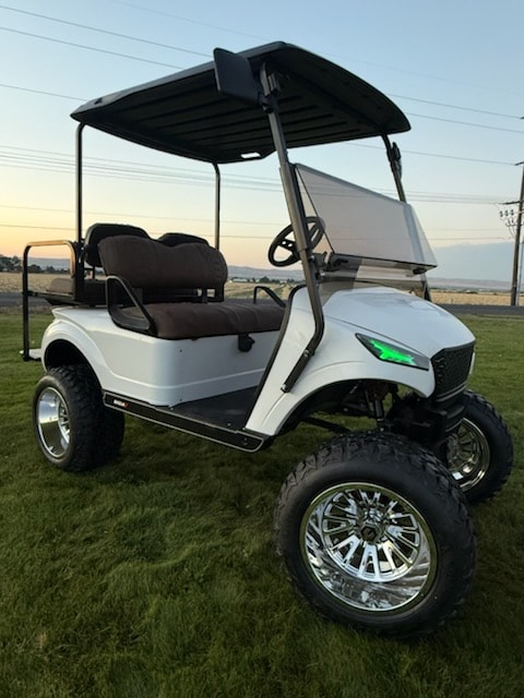 White lifted golf cart with chrome wheels on grass