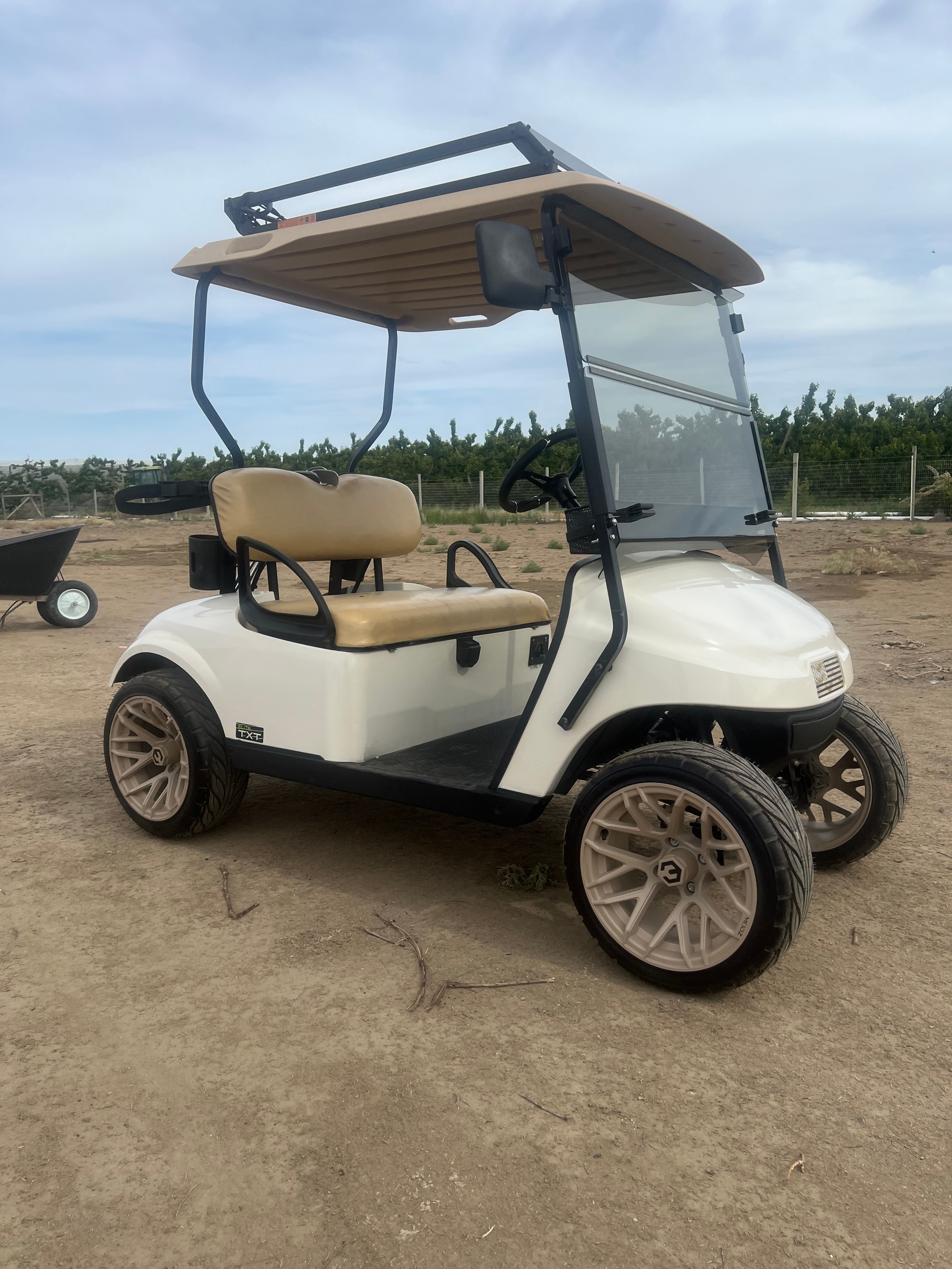 White golf cart with tan seats and custom wheels